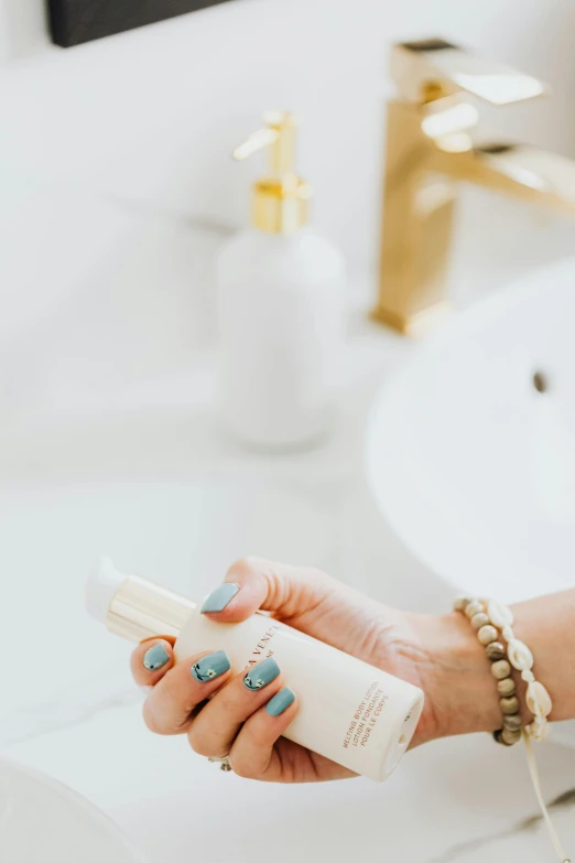 a woman holding a bottle of hand sanitizer in front of a bathroom sink, unsplash, minimalism, white with gold accents, photoshoot for skincare brand, on a white table, whitesmith