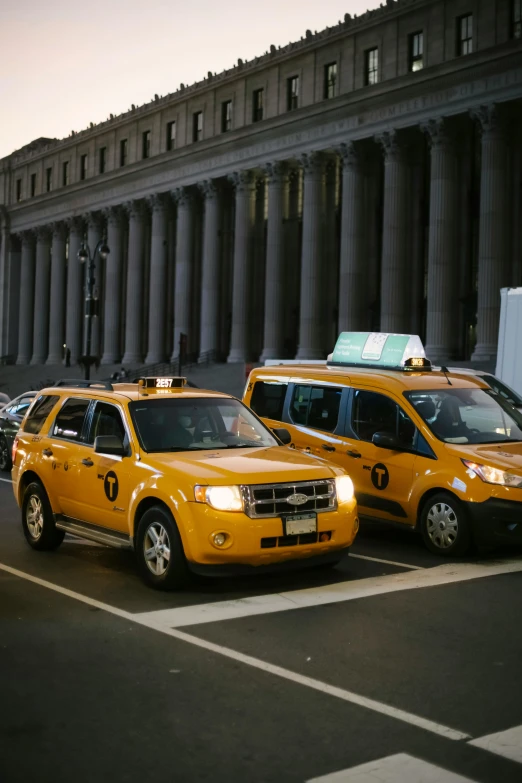 a group of taxi cabs parked in front of a building, in the evening