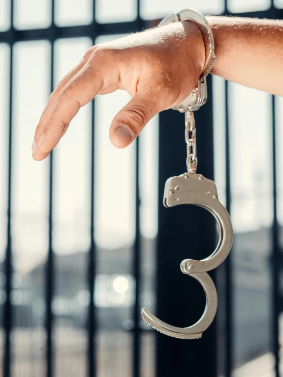 a close up of a person's hand holding a pair of handcuffs, cell bars, area 3, hanging, thumbnail