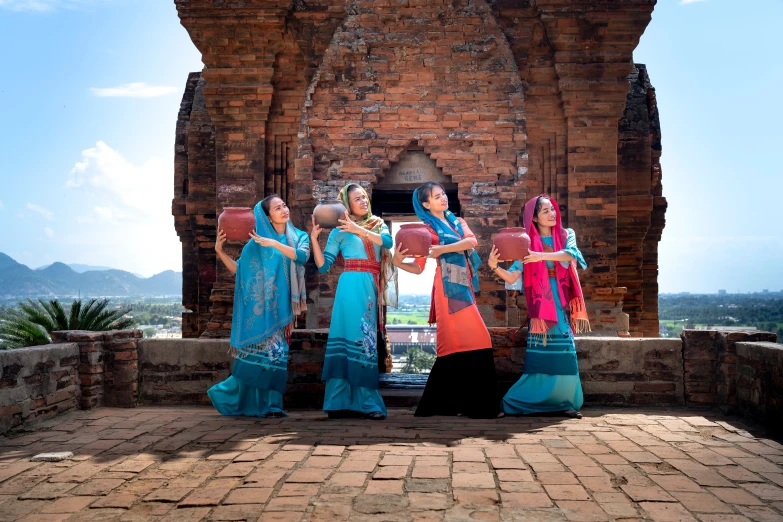a group of women standing in front of a brick building, inspired by Jin Nong, pexels contest winner, sukhothai costume, avatar image, sky blue, multicoloured