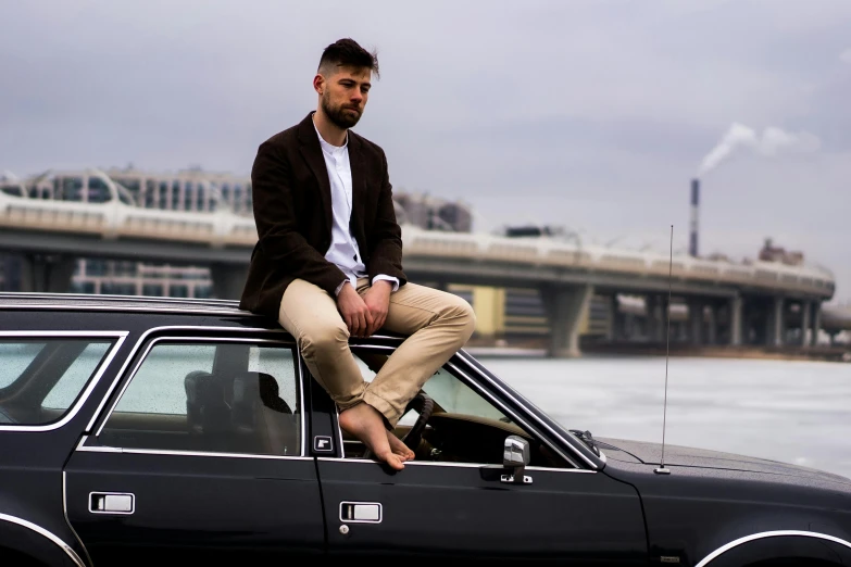 a man sitting on top of a black car, dapper, wearing only pants, zachary corzine, stoic pose