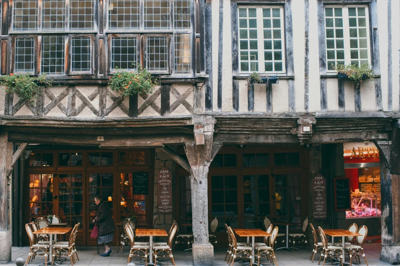 a building with tables and chairs in front of it, by Celia Fiennes, pexels contest winner, arts and crafts movement, medieval cities, gif, square, granville chandor