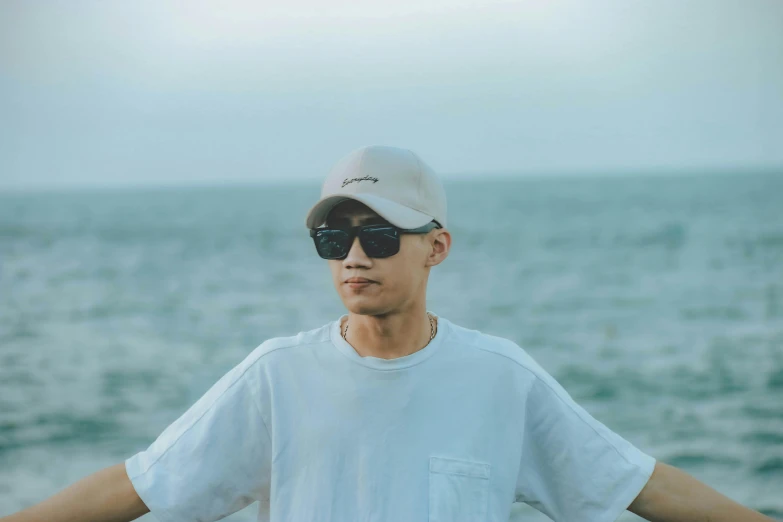 a man standing on top of a beach next to the ocean, by Jang Seung-eop, pexels contest winner, realism, wearing sunglasses and a cap, wearing off - white style, avatar image, headshot profile picture