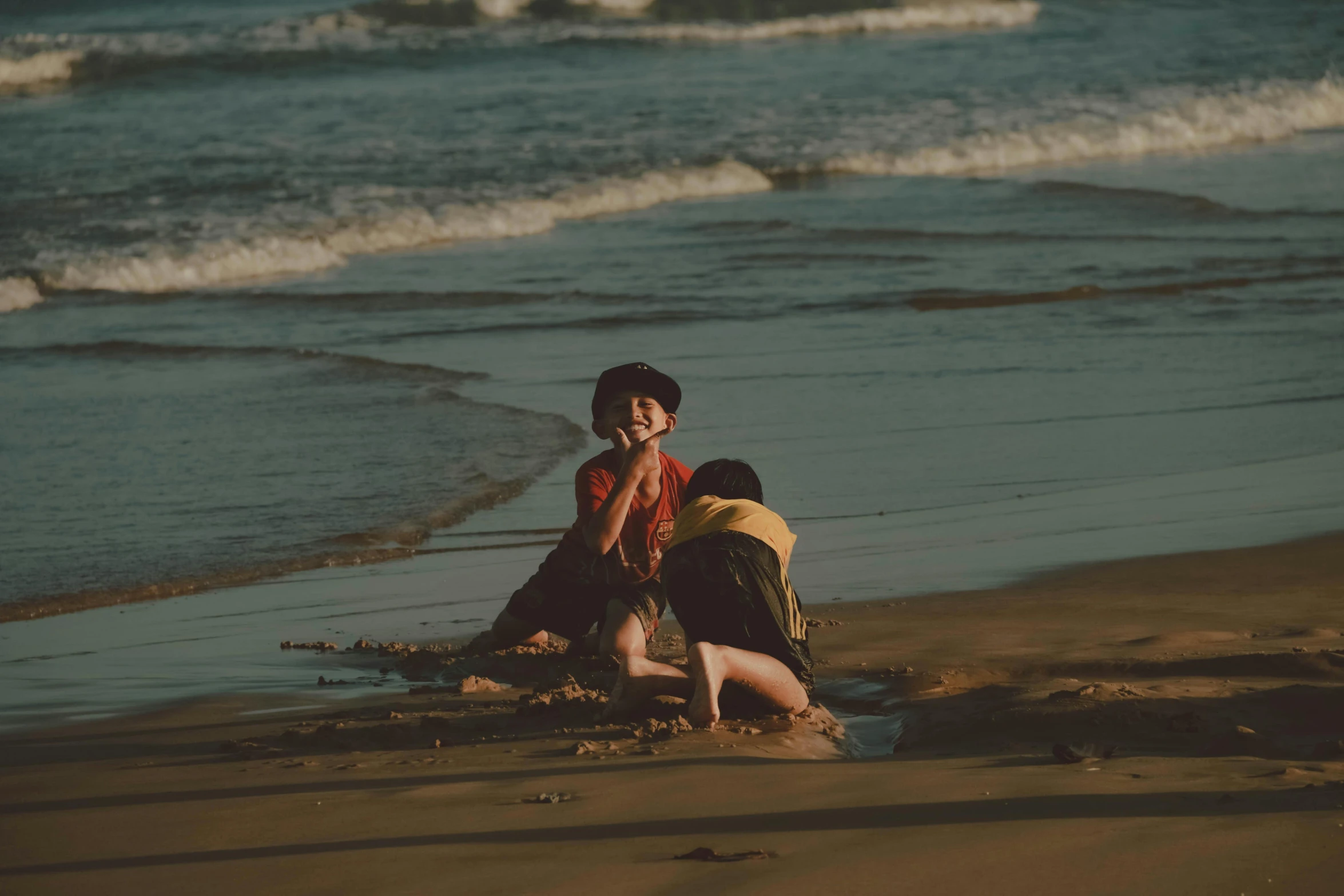 a couple of people sitting on top of a sandy beach, pexels contest winner, realism, kids playing, laughing menacingly, brown, lo fi