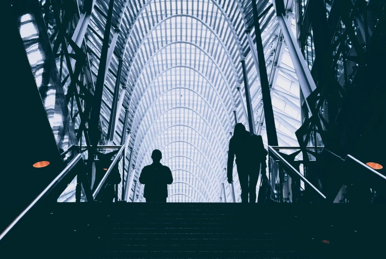 a person standing at the bottom of an escalator, by Carey Morris, pexels contest winner, hypermodernism, outlined silhouettes, giant majestic archways, two people, a photo of a man