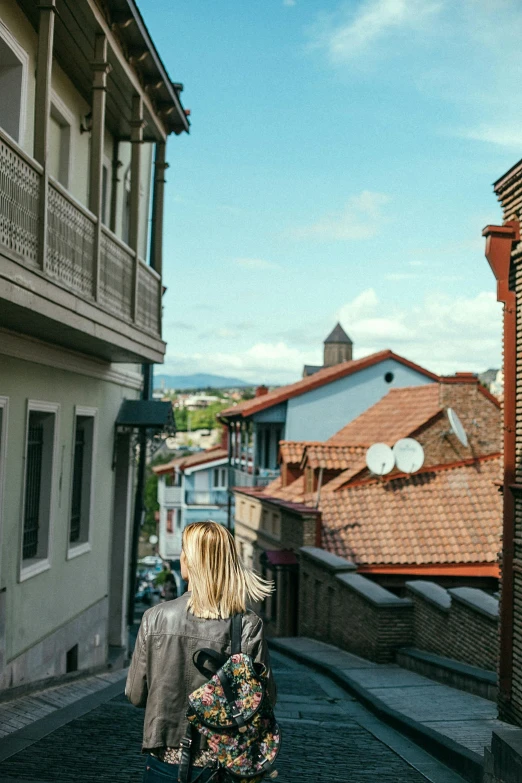 a woman walking down a narrow cobblestone street, skyline view from a rooftop, can basdogan, peaked wooden roofs, balcony