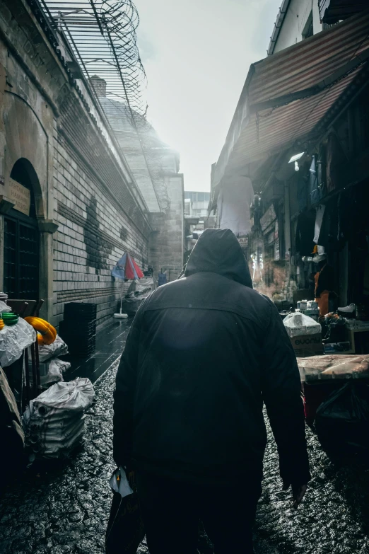 a man walking down a cobblestone street, an album cover, by Alessandro Allori, pexels contest winner, dystopian slums, wearing a dark hood, busy market, shot from the back