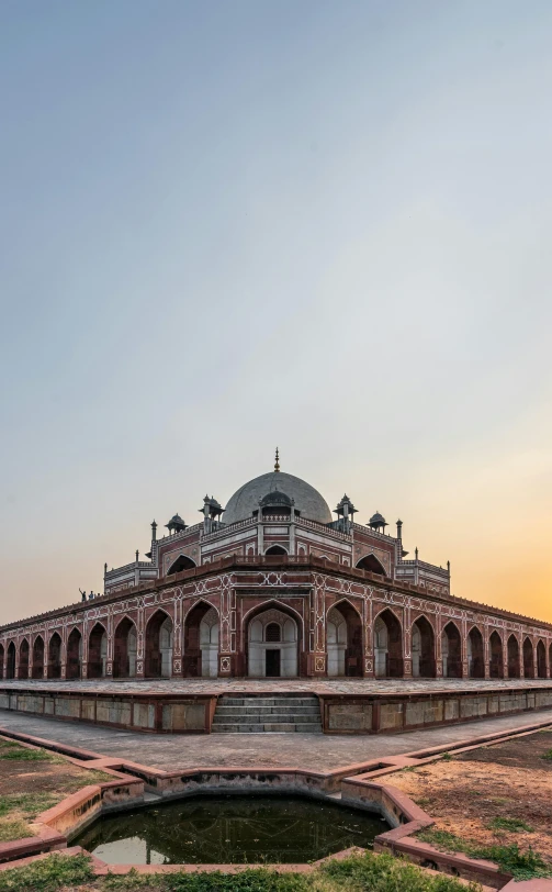 a large building sitting on top of a lush green field, by Bernardino Mei, with great domes and arches, at dawn, india, front facing