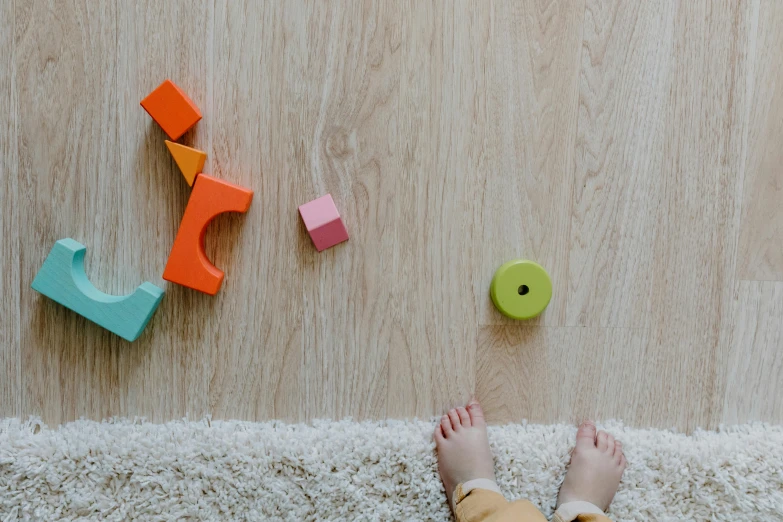 a person standing on the floor next to a pile of toys, pexels contest winner, wooden floors, background image, minimalistic design, kids playing