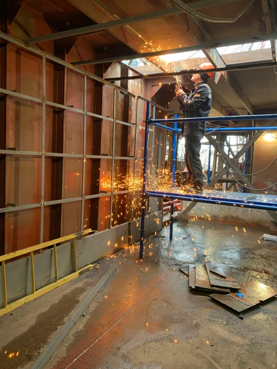 a man that is standing on a scaffolding, sparks flying, metal cladding wall, thumbnail, in a workshop