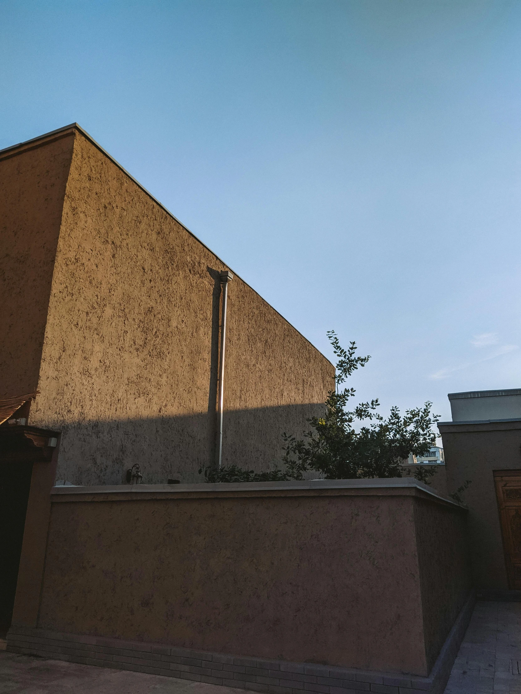 a man riding a skateboard up the side of a building, an album cover, by Attila Meszlenyi, unsplash, brutalism, rammed earth courtyard, late afternoon light, standing outside a house, light - brown wall