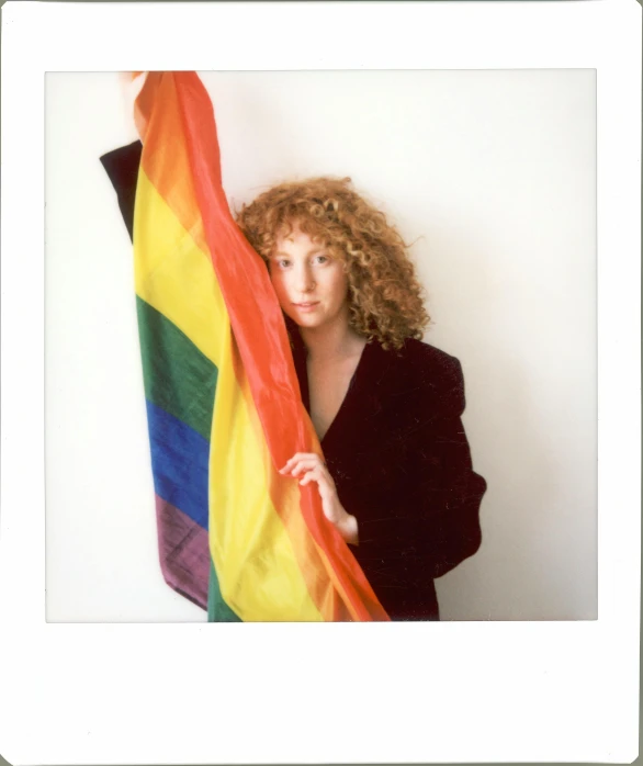 a woman with curly hair holding a rainbow flag, a polaroid photo, renaissance, press photo, andrée wallin, with blunt brown border, hr ginger