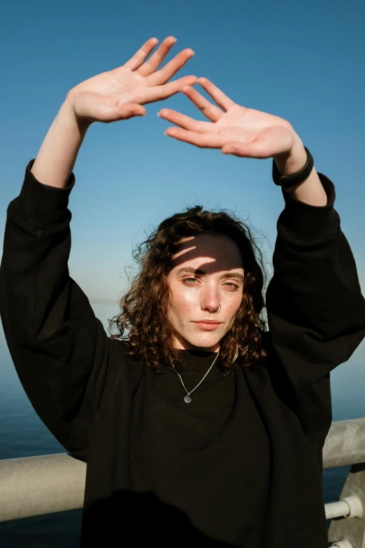a woman holding her hands up in the air, an album cover, pexels contest winner, antipodeans, wearing a black sweater, seaview, stoic pose, lorde