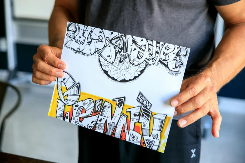 a man holding a piece of paper with graffiti on it, a drawing, by Jessie Algie, pexels contest winner, funny jumbled letters, highly detailed cover art, mekka, fresh from the printer