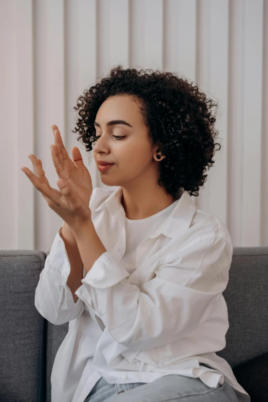 a woman sitting on a couch with her hands in the air, trending on pexels, arabesque, hands shielding face, curls, partially cupping her hands, mixed race woman