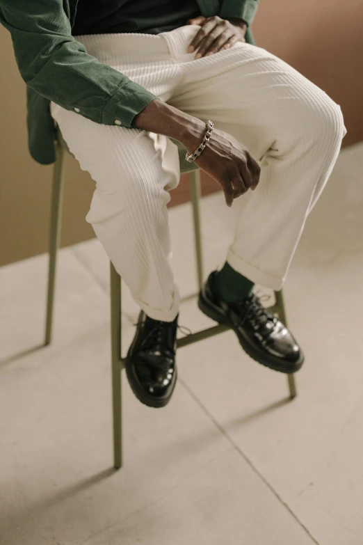 a man sitting on a chair talking on a cell phone, by Gavin Hamilton, trending on pexels, photorealism, green corduroy pants, white shoes, black loafers, man is with black skin