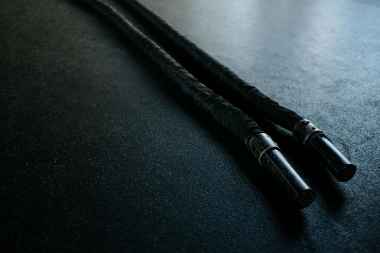 a couple of black cables sitting on top of a table, unsplash, sōsaku hanga, dragon staff, epic shafts, black textured, black floor