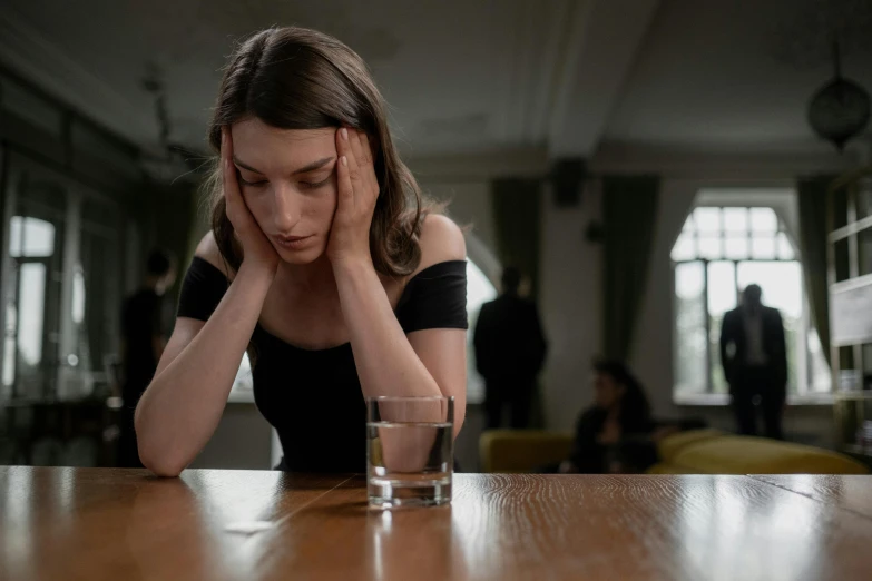 a woman sitting at a table with a glass of water, people crying, mental health, sitting on top a table, high forehead