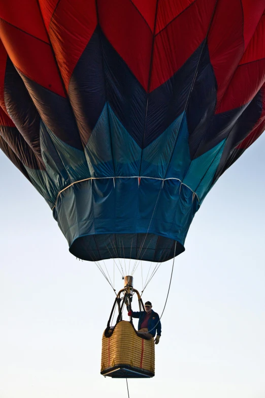 a red and blue hot air balloon flying in the sky, by Dave Melvin, happening, person in foreground, high-angle, canopy, landing lights