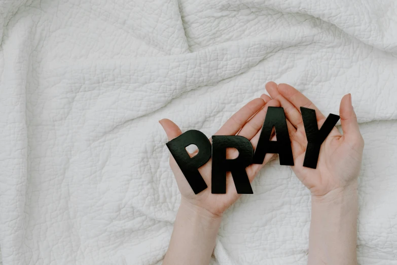 a person holding the word pray in their hands, by Carey Morris, trending on pexels, hurufiyya, lying down, 1 6 x 1 6, divine intervention, hey