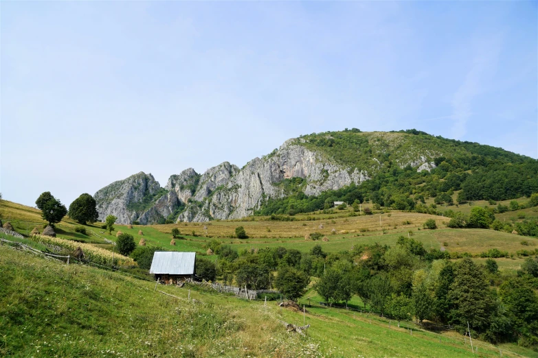 a house sitting on top of a lush green hillside, by Muggur, pexels contest winner, traditional romanian clothing, big sharp rock, barn in the background, limestone