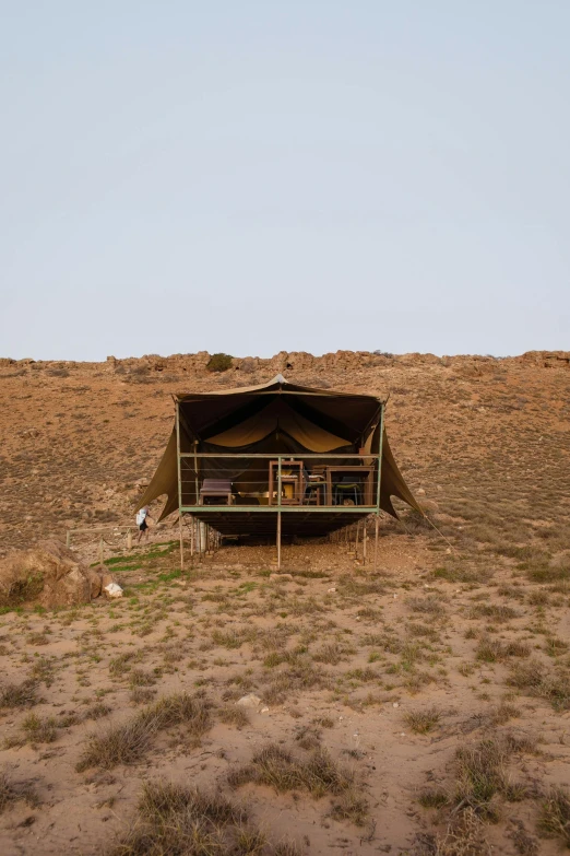a tent sitting on top of a dry grass covered field, hillside desert pavilion, symmetrical outpost, afar, full room view