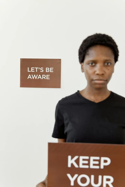 a woman holding a sign that says let's be aware, by Marina Abramović, emmanuel shiru, poop, panel, looking serious