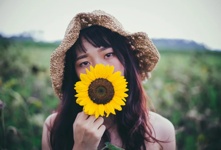 a woman holding a sunflower in front of her face, pexels contest winner, chinese girl, with hat, with freckles, 🌸 🌼 💮