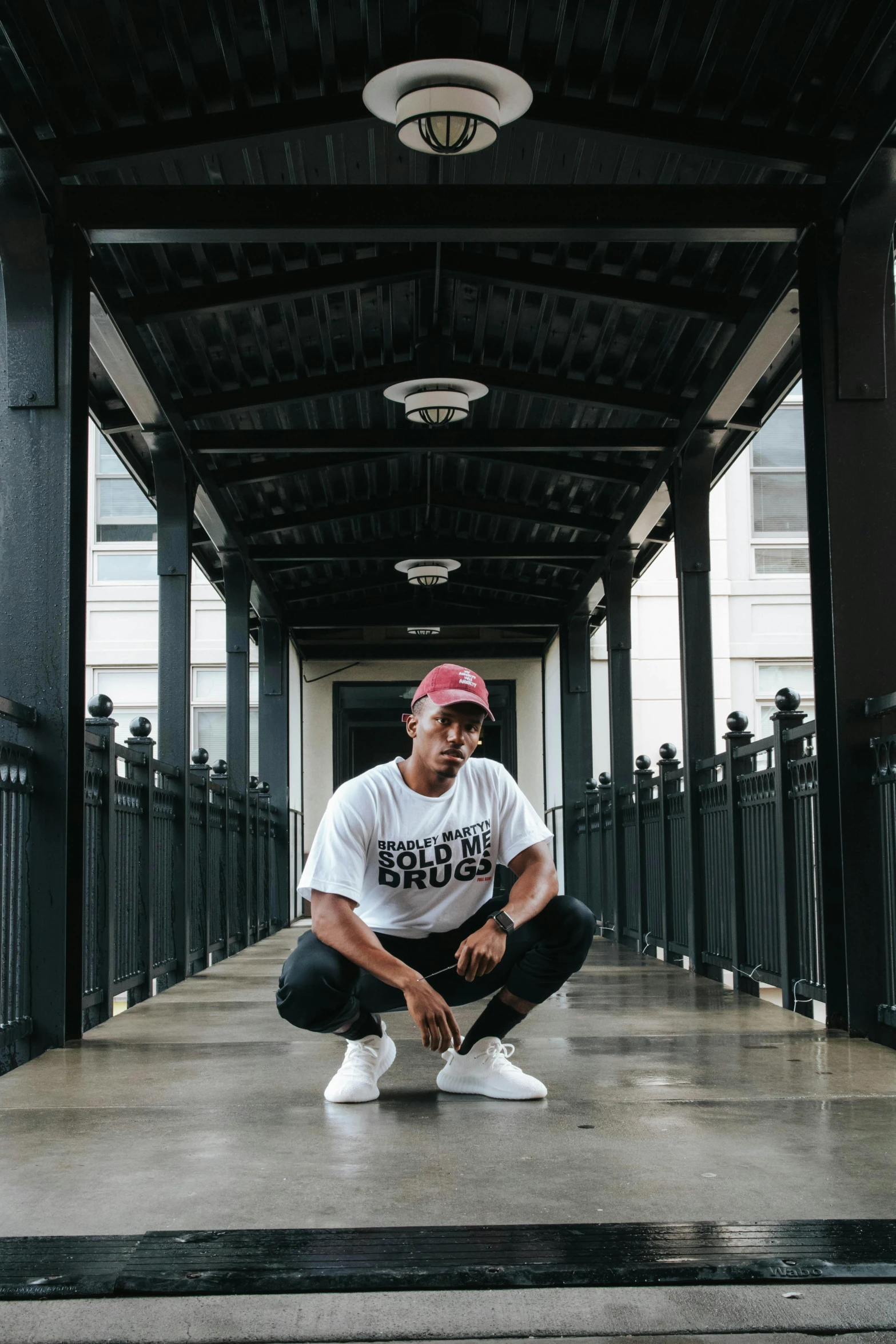 a man squatting in the middle of a walkway, black arts movement, maroon and white, posing solo, yzy gap, at college