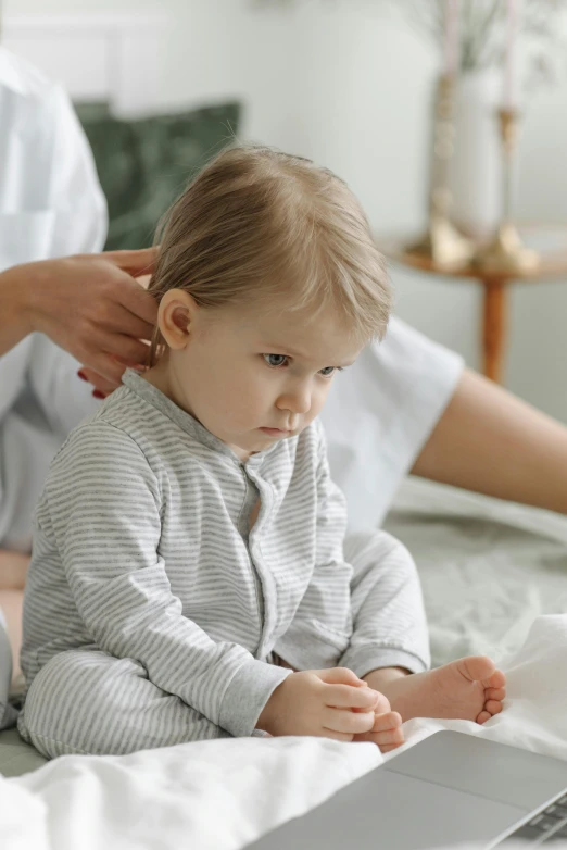 a woman sitting on top of a bed next to a baby, left ear, thinning hair, boy hair, acupuncture treatment