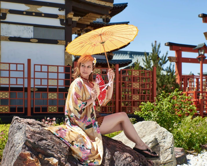 a woman sitting on a rock holding an umbrella, pale pink and gold kimono, himeji rivendell garden of eden, in the sun, tai costume