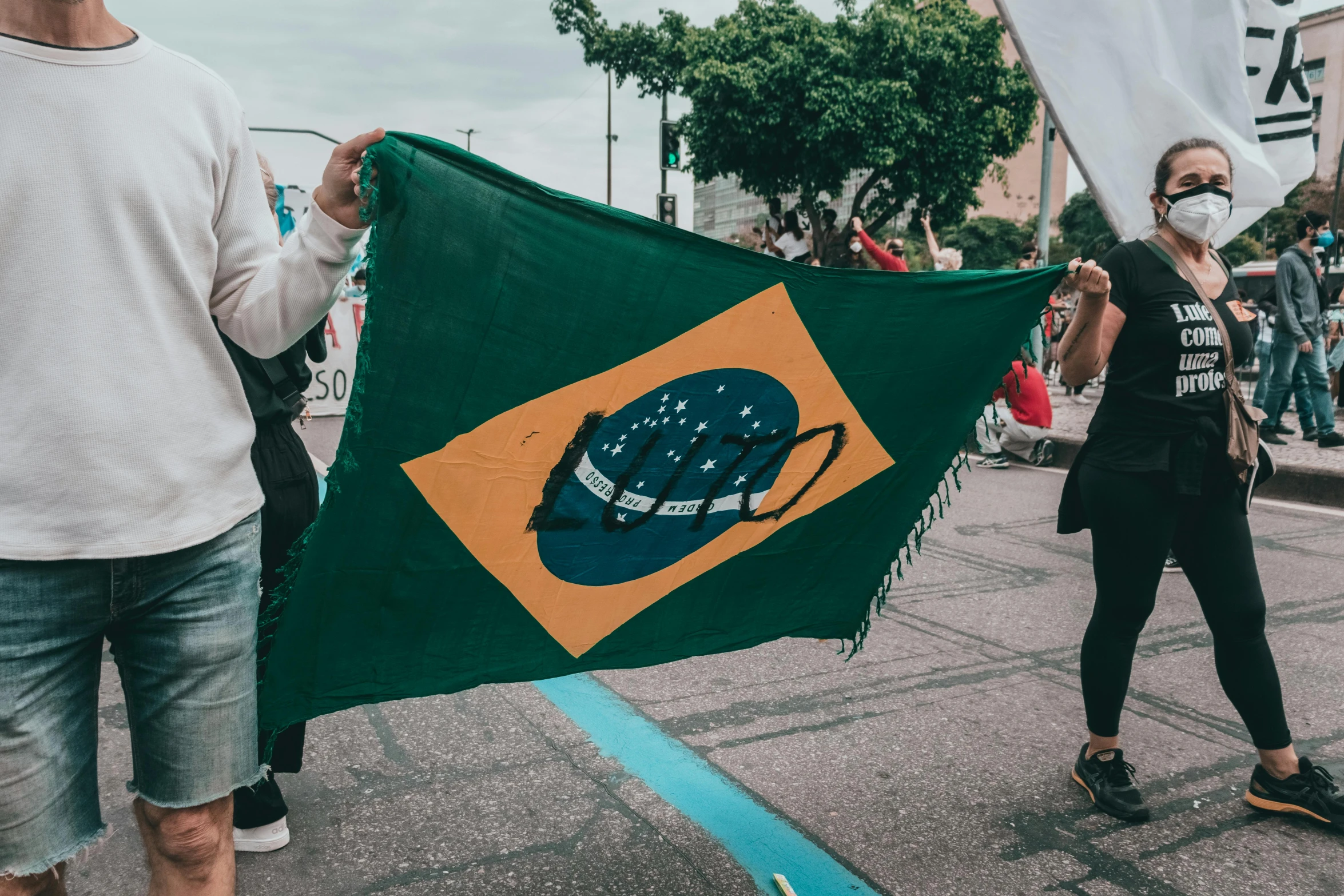 a group of people walking down a street holding flags, an album cover, by Amelia Peláez, trending on unsplash, brazilian flag, where a large, julian ope, show