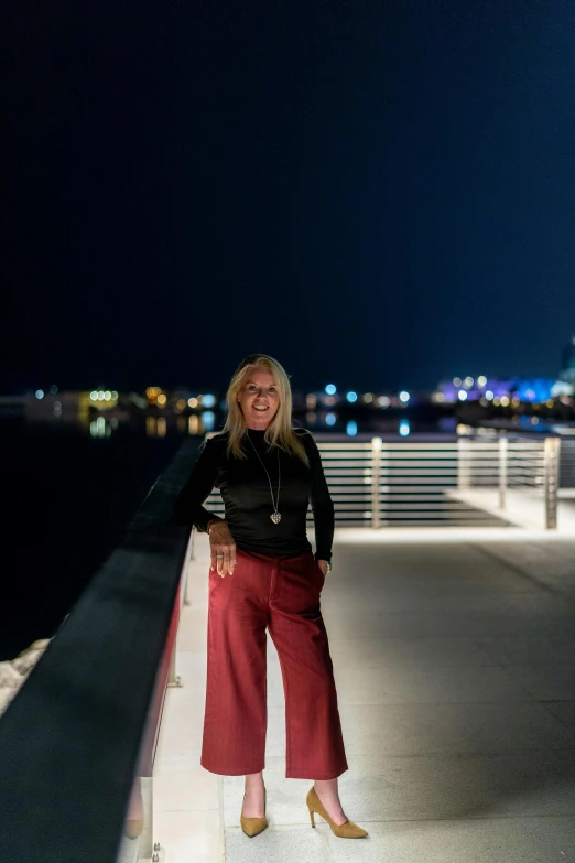 a woman standing on a bridge at night, by Bernie D’Andrea, standing beside the ocean, downtown jacksonville florida, 5 5 yo, high quality photo