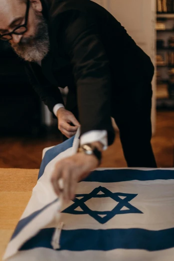 a man cutting a flag with a pair of scissors, inspired by Israel Tsvaygenbaum, trending on unsplash, medium shot portrait, 🚿🗝📝, on a table, an elegant