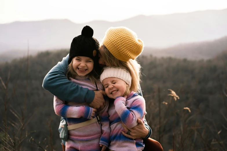two little girls hugging each other in a field, by Carey Morris, pexels contest winner, wearing a beanie, on top of a mountain, portrait of family of three, avatar image