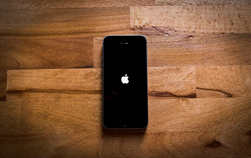 an iphone sitting on top of a wooden table, by Niko Henrichon, unsplash, square, apple logo, reboot, black