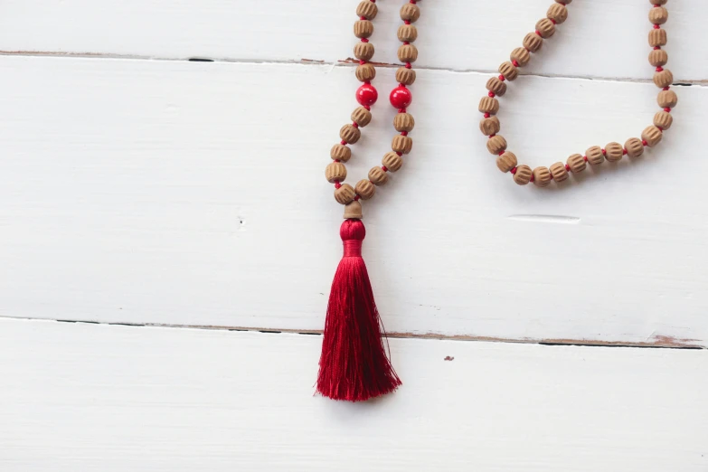 a wooden beaded necklace with a red tassel, inspired by Lü Ji, hurufiyya, sukhasana, focus on full - body, palm, cinnamon
