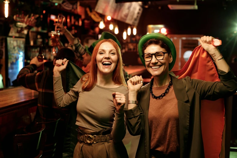 a couple of women standing next to each other, pexels, happening, in the pub, green flags, costumes, cheering