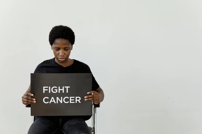 a woman sitting on a chair holding a sign that says fight cancer, pexels contest winner, man is with black skin, profile image, thumbnail, fighting posture