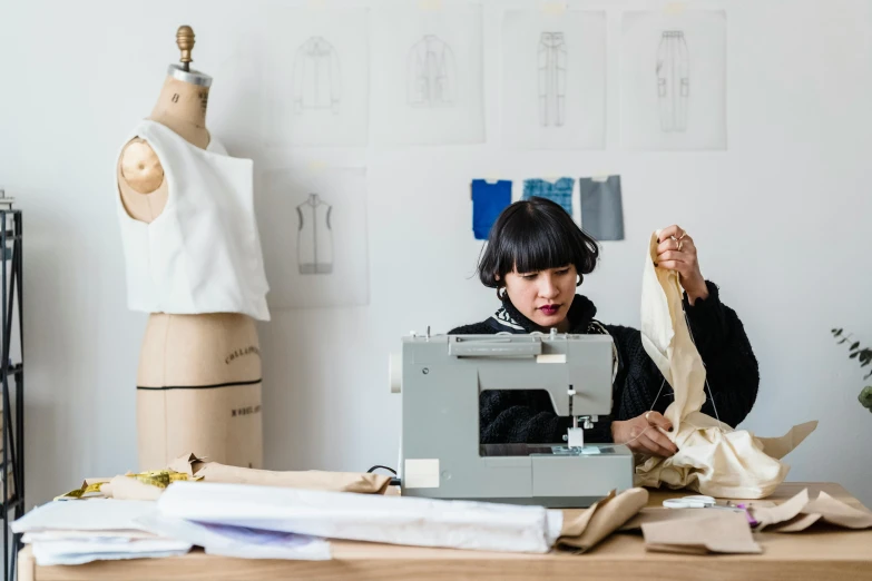 a woman sitting at a table working on a sewing machine, inspired by Ruth Jên, trending on unsplash, process art, costume design made with love, melbourne, wearing a designer top, cardboard