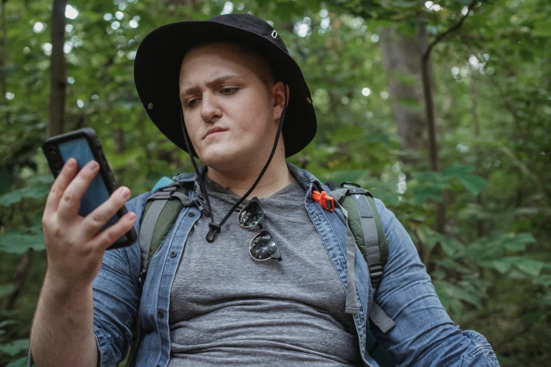 a man in a hat looking at his cell phone, trending on reddit, mr beast, in forest, an epic non - binary model, 2 5 6 x 2 5 6 pixels