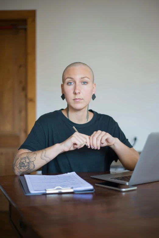 a woman sitting in front of a laptop computer, antipodeans, shaved hair, zachary corzine, compassionate, high resolution photo