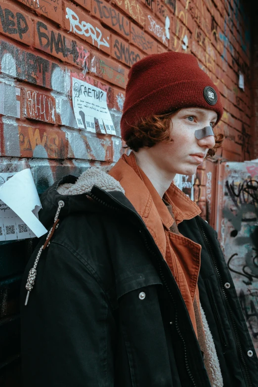 a man standing in front of a wall covered in graffiti, an album cover, trending on pexels, red haired teen boy, beanie, very very very pale skin, headshot profile picture