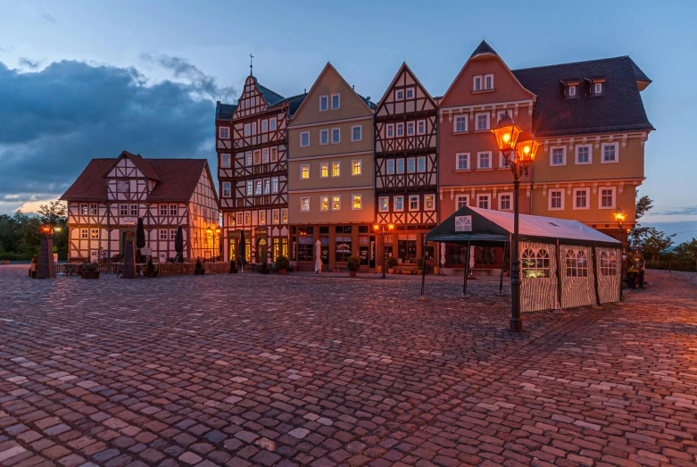 a group of buildings sitting on top of a cobblestone street, by Julia Pishtar, unsplash contest winner, art nouveau, lower saxony, calm evening, square, sunken square