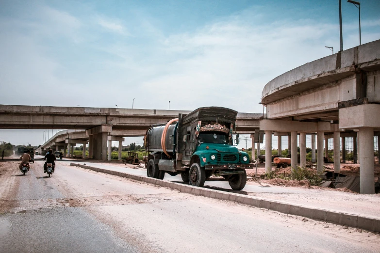 a green truck driving down a street next to a bridge, by Sven Erixson, pexels contest winner, rural wastelands, cement, amr elshamy, post-war
