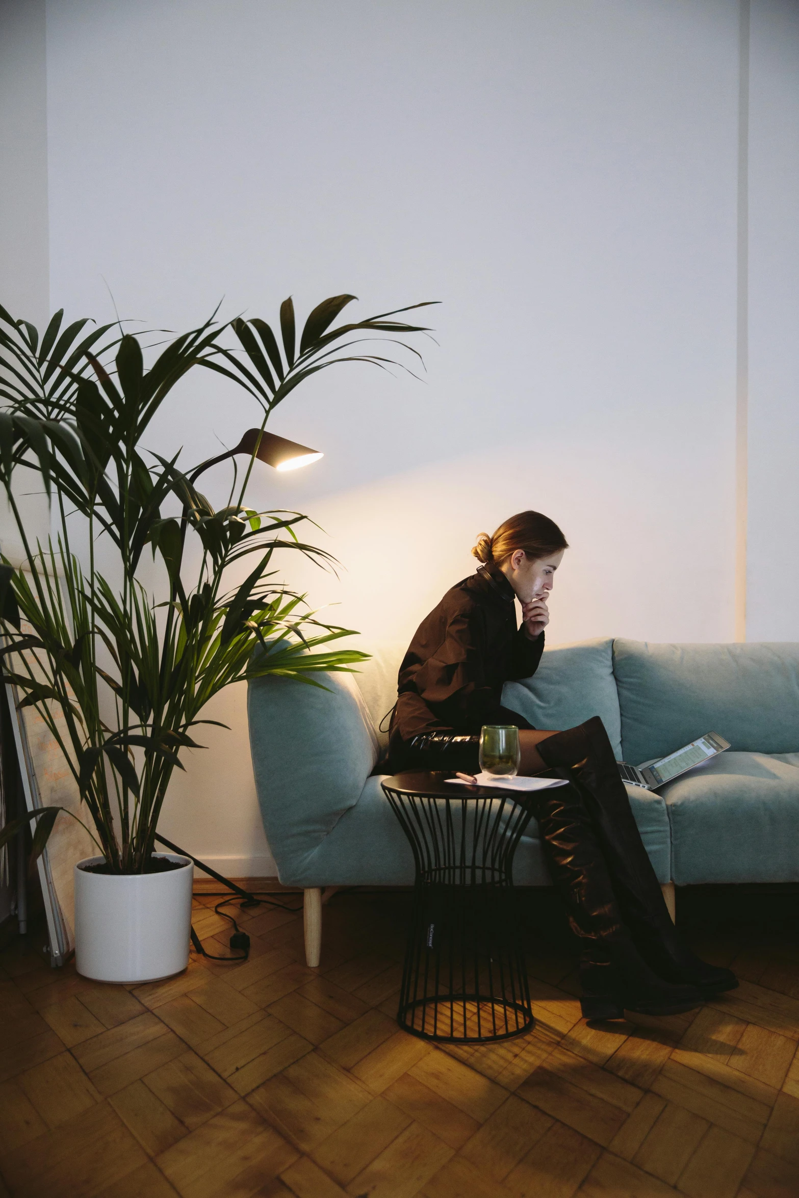 a woman sitting on a couch next to a potted plant, inspired by Elsa Bleda, trending on unsplash, lights off, in an office, ignant, reading nook