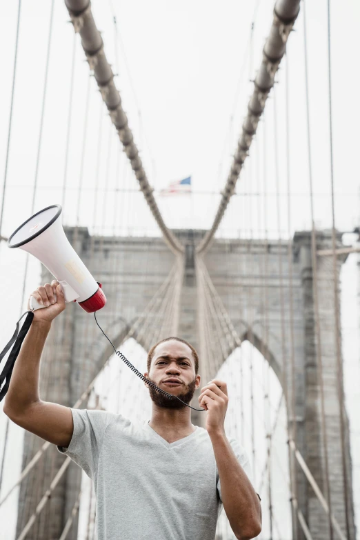 a man holding a megaphone in front of a bridge, by Amos Ferguson, pexels contest winner, black arts movement, humans of new york, 🚿🗝📝, yzy gap, patriotism