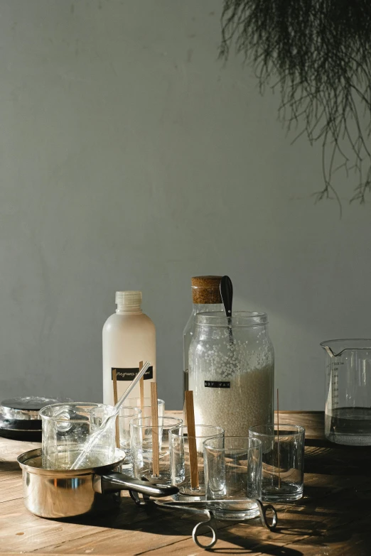 a table topped with bottles and glasses on top of a wooden table, a still life, inspired by Hiromitsu Takahashi, unsplash, milk bath photography, dwell, scientific glassware, on textured base; store website