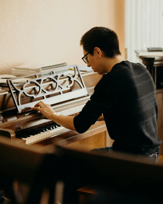 a man sitting at a piano in a living room, inspired by Bryan Organ, pexels contest winner, non-binary, asian man, profile image, sitting on a mocha-colored table