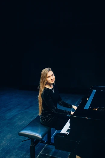 a woman sitting at a piano in a dark room, an album cover, inspired by Julia Pishtar, unsplash, performing on stage, plain background, very slightly smiling, andrey gordeev